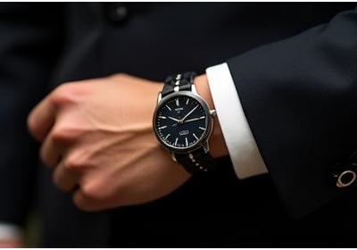 Elegant braided leather bracelet with a discreet metal clasp, adjacent to a classic wristwatch.